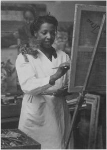 Loïs Mailou Jones painting in her Paris studio in 1937 with kitten supervising from her shoulder.